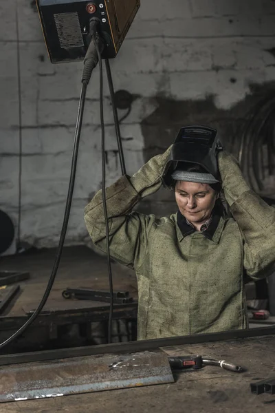 Retrato de la trabajadora manual quitándose el casco protector después del trabajo en el taller - foto de stock