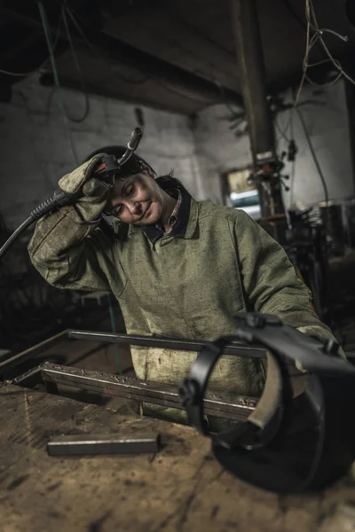 Mujer soldadora cansada sosteniendo la antorcha de soldadura en el taller - foto de stock