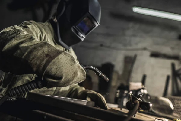 Vista laterale del saldatore nell'usura protettiva del lavoro che lavora con la torcia di saldatura in officina — Foto stock