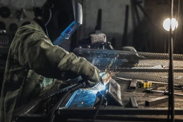 Vista laterale del saldatore nell'usura protettiva del lavoro che lavora con la torcia di saldatura in officina — Foto stock