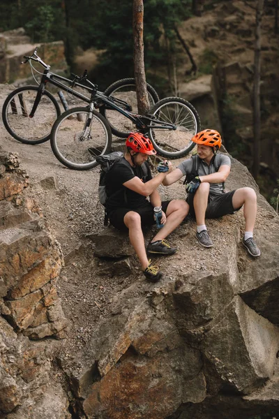 Blick aus der Vogelperspektive auf junge Trial-Biker, die sich nach der Fahrt auf felsigen Klippen entspannen und Hände schütteln — Stockfoto