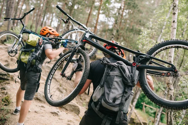 Vue arrière de jeunes motards d'essai portant des vélos sur le dos à la forêt et montant — Photo de stock