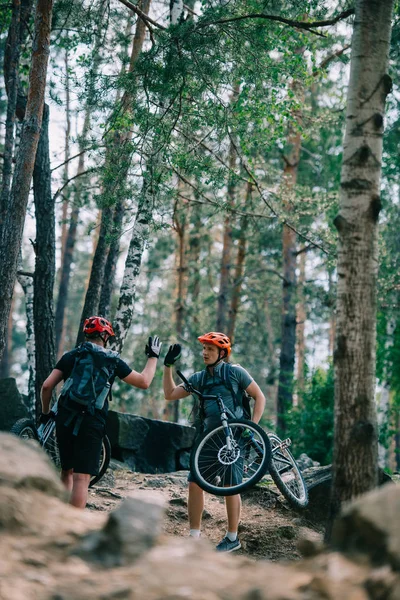 Jovens motociclistas julgamento dando alta cinco na bela floresta — Fotografia de Stock