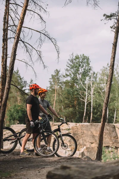 Handsome young trial bikers standing on cliff with bicycles — Stock Photo