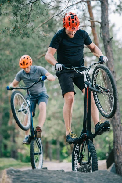 Active young trial bikers performing stunts on boulders — Stock Photo