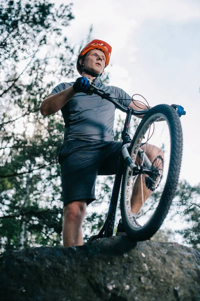 Bottom view of handsome trial biker standing on rock outdoors — Stock Photo