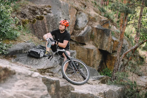 Giovane trial biker rilassante su rocce con bicicletta all'aperto — Foto stock