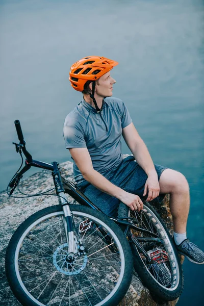 Riflessivo giovane biker di prova rilassante sulla scogliera rocciosa sopra l'acqua — Foto stock