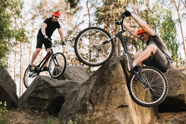 Jóvenes ciclistas de trial activos cabalgando sobre rocas al aire libre - foto de stock
