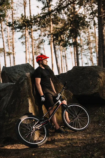 Young trial biker leaning back on rocks outdoors in forest — Stock Photo