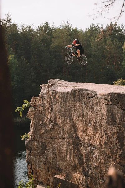 Trial biker jumping on bicycle over rocky cliff outdoors in forest — Stock Photo