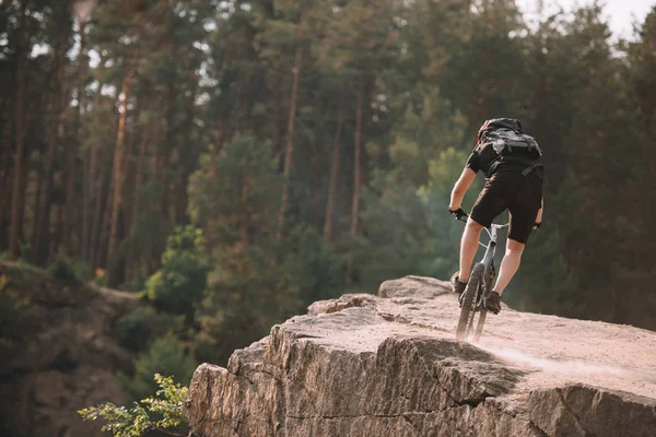 Vista trasera del joven ciclista de trial cabalgando sobre rocas al aire libre - foto de stock