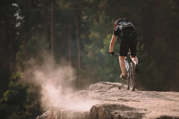 Rear view of young trial biker riding on rocks outdoors — Stock Photo