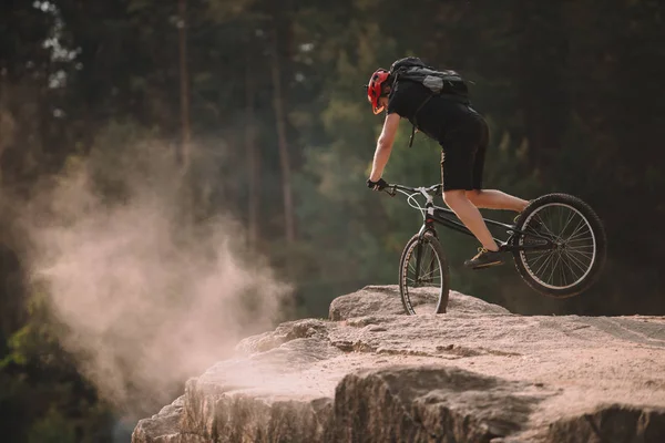 Young trial biker balancing on front wheel on rocks outdoors — Stock Photo