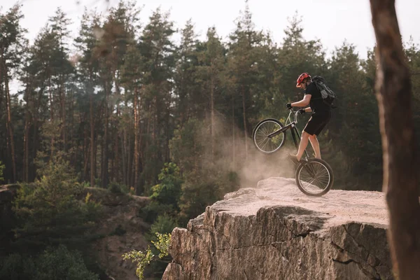 Trial-Biker balanciert auf Hinterrad auf Felsen im Freien — Stockfoto