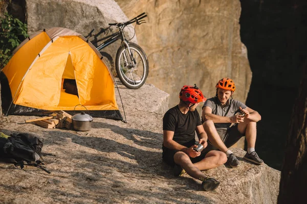 Happy young bike travellers with canned food sitting on cliff — Stock Photo