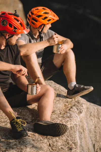 Viajeros activos comiendo comida enlatada en un acantilado rocoso - foto de stock