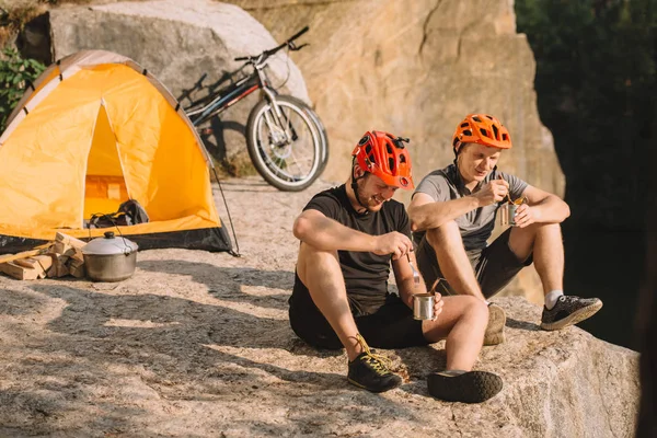 Ciclistas de prueba feliz comer comida enlatada en acampar en el acantilado - foto de stock