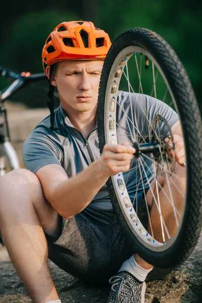 Close-up shot of young trial biker examining bike wheel outdoors — Stock Photo