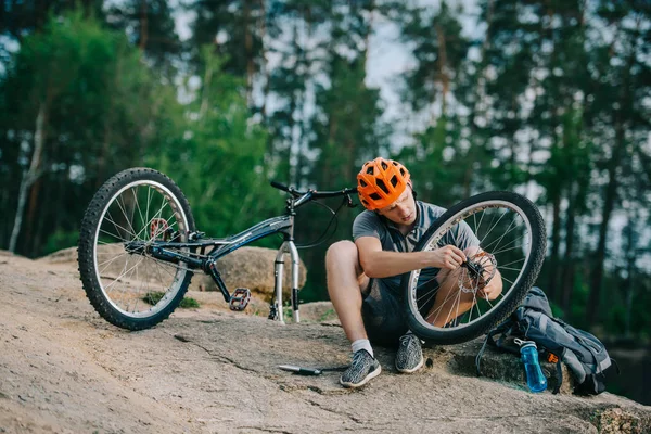 Jovem motociclista julgamento examinando roda de bicicleta ao ar livre — Fotografia de Stock