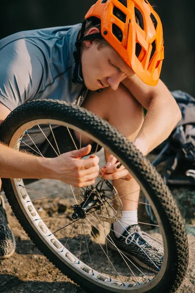 Close-up shot of young trial biker fixing bicycle wheel outdoors — Stock Photo
