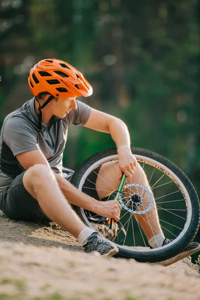 Handsome young trial biker pumping wheel of bicycle outdoors — Stock Photo