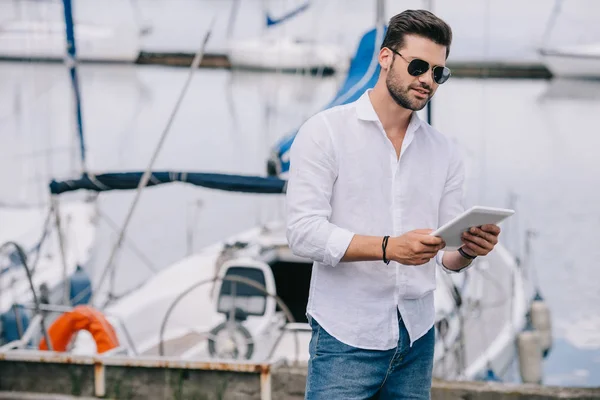 Handsome young man in sunglasses using digital tablet at seaside — Stock Photo