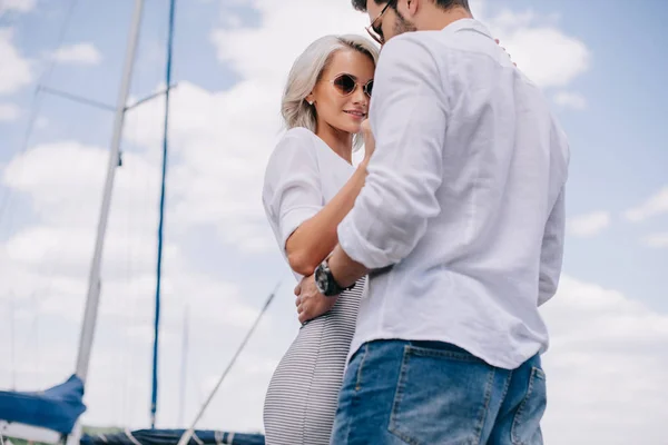Low angle view of beautiful stylish young couple in sunglasses hugging on yacht — Stock Photo