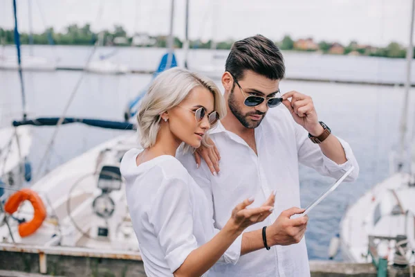 Beautiful stylish young couple in sunglasses using digital tablet on yacht — Stock Photo