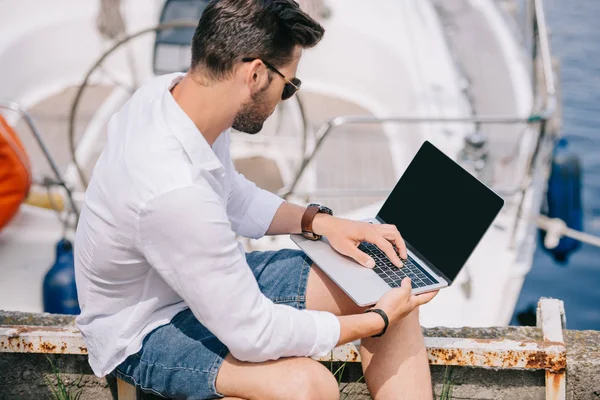 Young man in sunglasses using laptop with blank screen at seaside — Stock Photo