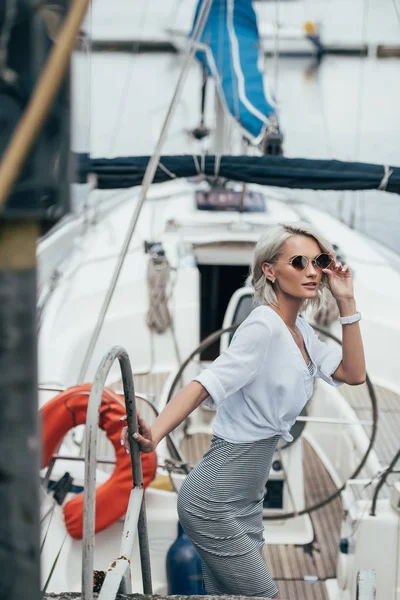 Beautiful young woman in sunglasses looking at camera on yacht — Stock Photo