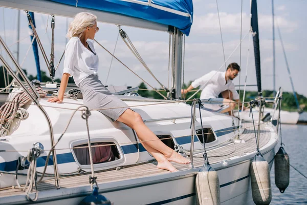 Beautiful young woman sitting on yacht and looking at man behind — Stock Photo