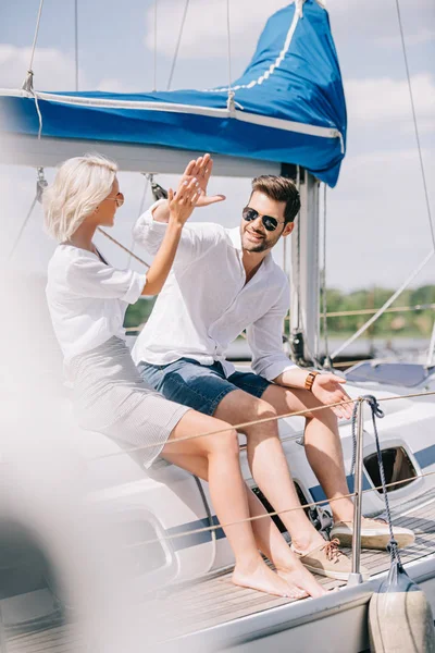 Счастливая молодая пара дает пять, сидя вместе на яхте — стоковое фото