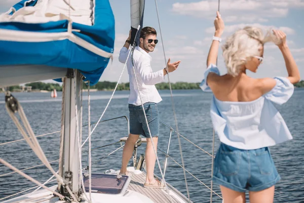 Улыбающийся молодой человек в солнечных очках, смотрящий на красивую девушку на яхте — стоковое фото