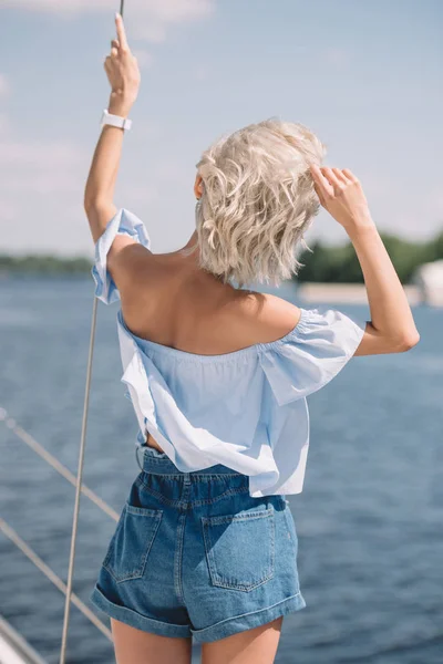 Vue arrière de la jeune femme blonde regardant loin tout en se tenant sur le yacht — Photo de stock