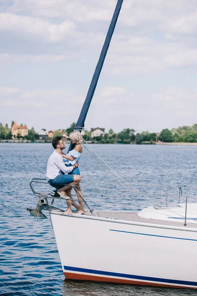 Seitenansicht eines schönen glücklichen jungen Paares, das auf einer Yacht sitzt und sich umarmt — Stockfoto