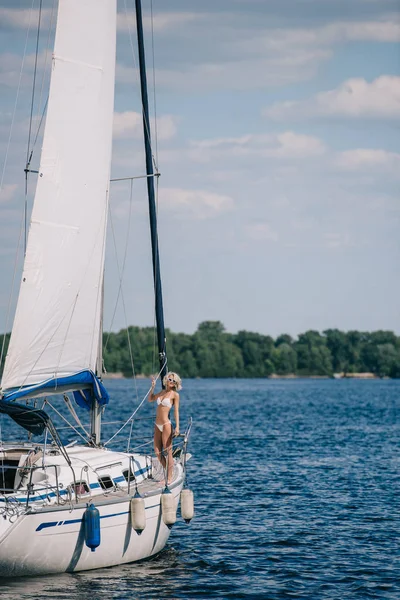 Belle jeune femme blonde en bikini debout sur le yacht — Photo de stock