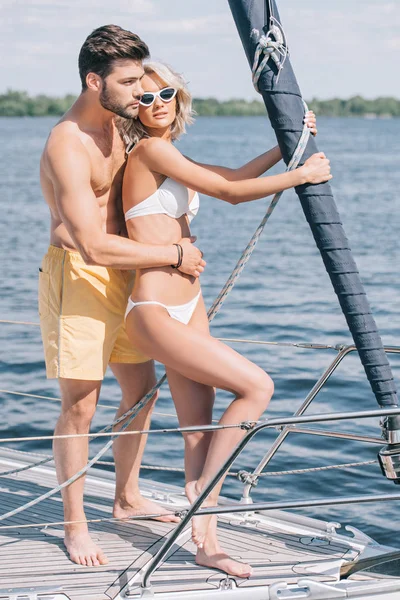 Schönes junges Paar in Badebekleidung, das sich umarmt, während es zusammen auf einer Jacht steht — Stockfoto