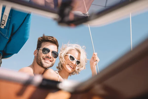 Selektiver Fokus eines glücklichen jungen Paares mit Sonnenbrille, das in die Kamera lächelt, während es Zeit auf einer Jacht verbringt — Stockfoto