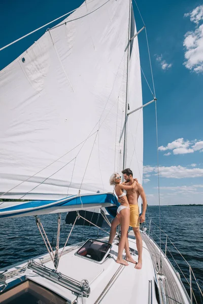 Sorridente giovane coppia in costume da bagno che abbraccia su yacht — Foto stock