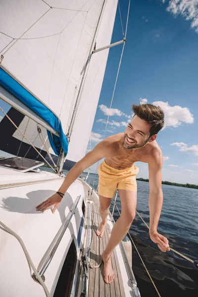 Smiling shirtless man in swim trunks running on yacht — Stock Photo