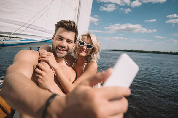 Smiling young couple taking selfie on smartphone on yacht — Stock Photo