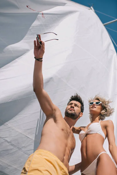 Low angle view of shirtless man in swimwear pointing by hand to girlfriend on yacht — Stock Photo