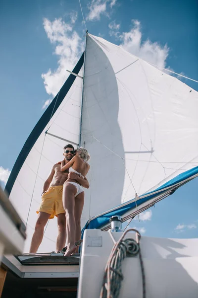 Низький кут зору без сорочки чоловіка в сонцезахисних окулярах, що приймає дівчину в бікіні на яхті — стокове фото