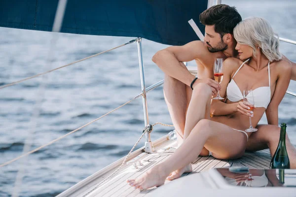 Giovane coppia in costume da bagno seduta con bicchieri di champagne sullo yacht — Foto stock