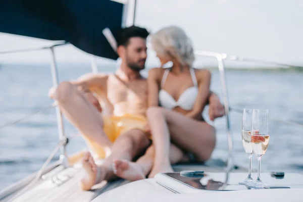 Selective focus of champagne glasses and couple sitting behind on yacht — Stock Photo