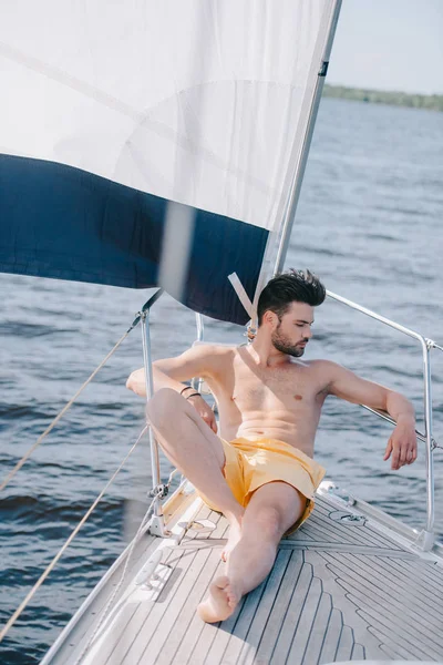 Shirtless muscular man in swim trunks having sunbath on yacht — Stock Photo