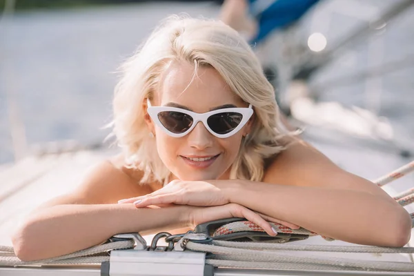 Selective focus of attractive young woman in sunglasses laying on yacht — Stock Photo