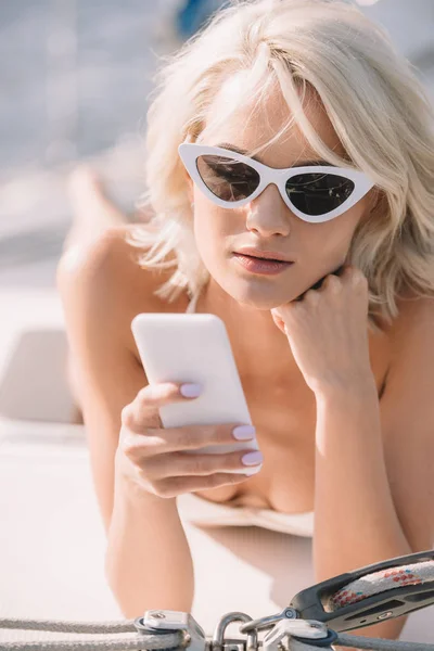 Mujer atractiva joven en gafas de sol con smartphone y yate - foto de stock