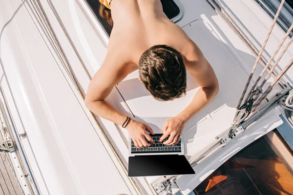 Overhead view of shirtless man using laptop with blank screen on yacht — Stock Photo